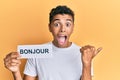 Young handsome african american man holding bonjour french greeting word pointing thumb up to the side smiling happy with open