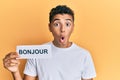 Young handsome african american man holding bonjour french greeting word scared and amazed with open mouth for surprise, disbelief