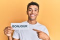 Young handsome african american man holding bonjour french greeting word smiling happy pointing with hand and finger