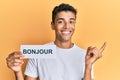 Young handsome african american man holding bonjour french greeting word smiling happy pointing with hand and finger to the side