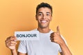 Young handsome african american man holding bonjour french greeting word smiling happy and positive, thumb up doing excellent and