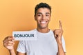 Young handsome african american man holding bonjour french greeting word smiling with an idea or question pointing finger with