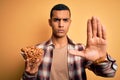 Young handsome african american man holding bowl with german baked pretzels with open hand doing stop sign with serious and Royalty Free Stock Photo