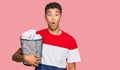 Young handsome african american man holding paper bin full of crumpled papers scared and amazed with open mouth for surprise, Royalty Free Stock Photo