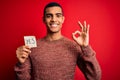 Young handsome african american man holding reminder paper with yes message doing ok sign with fingers, excellent symbol