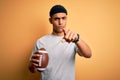 Young handsome african american man holding rugby ball over isolated yellow background pointing with finger to the camera and to Royalty Free Stock Photo