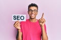 Young handsome african american man holding seo message paper smiling with an idea or question pointing finger with happy face, Royalty Free Stock Photo