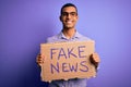 Young handsome african american man protesting holding banner with fake news message with a happy face standing and smiling with a