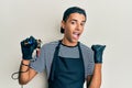 Young handsome african american man tattoo artist wearing professional uniform and gloves holding tattooer machine smiling with Royalty Free Stock Photo