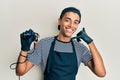 Young handsome african american man tattoo artist wearing professional uniform and gloves holding tattooer machine smiling doing Royalty Free Stock Photo