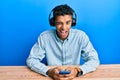 Young handsome african american man using smartphone wearing headphones winking looking at the camera with sexy expression, Royalty Free Stock Photo