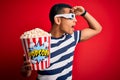 Young handsome african american man watching movie using 3d glasses eating popcorns very happy and smiling looking far away with Royalty Free Stock Photo