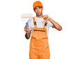 Young handsome african american man wearing cap and painter clothes holding painting roll with angry face, negative sign showing