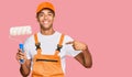 Young handsome african american man wearing cap and painter clothes holding painting roll pointing finger to one self smiling Royalty Free Stock Photo