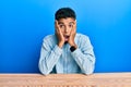 Young handsome african american man wearing casual clothes sitting on the table afraid and shocked, surprise and amazed expression Royalty Free Stock Photo