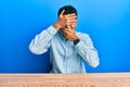 Young handsome african american man wearing casual clothes sitting on the table covering eyes and mouth with hands, surprised and Royalty Free Stock Photo