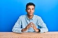 Young handsome african american man wearing casual clothes sitting on the table hands together and fingers crossed smiling relaxed Royalty Free Stock Photo