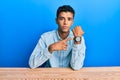 Young handsome african american man wearing casual clothes sitting on the table in hurry pointing to watch time, impatience, Royalty Free Stock Photo