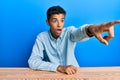 Young handsome african american man wearing casual clothes sitting on the table pointing with finger surprised ahead, open mouth Royalty Free Stock Photo