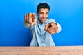 Young handsome african american man wearing casual clothes sitting on the table pointing to you and the camera with fingers, Royalty Free Stock Photo