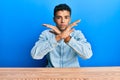 Young handsome african american man wearing casual clothes sitting on the table rejection expression crossing arms doing negative Royalty Free Stock Photo