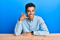Young handsome african american man wearing casual clothes sitting on the table smiling doing phone gesture with hand and fingers Royalty Free Stock Photo