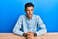 Young handsome african american man wearing casual clothes sitting on the table winking looking at the camera with sexy Royalty Free Stock Photo