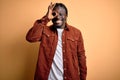 Young handsome african american man wearing casual jacket standing over yellow background doing ok gesture with hand smiling, eye Royalty Free Stock Photo