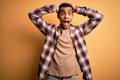 Young handsome african american man wearing casual shirt standing over yellow background Crazy and scared with hands on head, Royalty Free Stock Photo