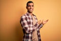 Young handsome african american man wearing casual shirt standing over yellow background Inviting to enter smiling natural with Royalty Free Stock Photo