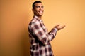 Young handsome african american man wearing casual shirt standing over yellow background pointing aside with hands open palms Royalty Free Stock Photo