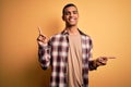 Young handsome african american man wearing casual shirt standing over yellow background smiling confident pointing with fingers Royalty Free Stock Photo