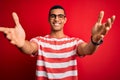 Young handsome african american man wearing casual striped t-shirt and glasses looking at the camera smiling with open arms for Royalty Free Stock Photo