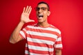 Young handsome african american man wearing casual striped t-shirt and glasses shouting and screaming loud to side with hand on Royalty Free Stock Photo