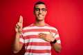 Young handsome african american man wearing casual striped t-shirt and glasses smiling swearing with hand on chest and fingers up, Royalty Free Stock Photo