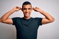 Young handsome african american man wearing casual t-shirt standing over white background Smiling pulling ears with fingers, funny Royalty Free Stock Photo