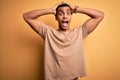 Young handsome african american man wearing casual t-shirt standing over yellow background Crazy and scared with hands on head, Royalty Free Stock Photo