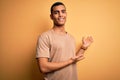 Young handsome african american man wearing casual t-shirt standing over yellow background Inviting to enter smiling natural with Royalty Free Stock Photo