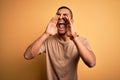 Young handsome african american man wearing casual t-shirt standing over yellow background Shouting angry out loud with hands over Royalty Free Stock Photo