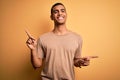 Young handsome african american man wearing casual t-shirt standing over yellow background smiling confident pointing with fingers Royalty Free Stock Photo
