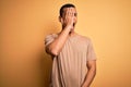 Young handsome african american man wearing casual t-shirt standing over yellow background Yawning tired covering half face, eye Royalty Free Stock Photo