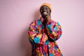 Young handsome african american man wearing colorful coat and cap over pink background looking confident at the camera with smile Royalty Free Stock Photo