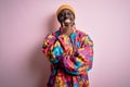 Young handsome african american man wearing colorful coat and cap over pink background looking confident at the camera smiling Royalty Free Stock Photo