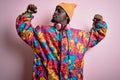 Young handsome african american man wearing colorful coat and cap over pink background showing arms muscles smiling proud Royalty Free Stock Photo