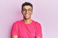 Young handsome african american man wearing glasses over pink background happy face smiling with crossed arms looking at the Royalty Free Stock Photo