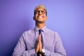 Young handsome african american man wearing golden crown of king over purple background begging and praying with hands together