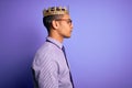 Young handsome african american man wearing golden crown of king over purple background looking to side, relax profile pose with Royalty Free Stock Photo