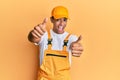 Young handsome african american man wearing handyman uniform over yellow background approving doing positive gesture with hand, Royalty Free Stock Photo