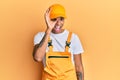 Young handsome african american man wearing handyman uniform over yellow background doing ok gesture with hand smiling, eye Royalty Free Stock Photo