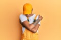 Young handsome african american man wearing handyman uniform over yellow background hugging oneself happy and positive, smiling Royalty Free Stock Photo